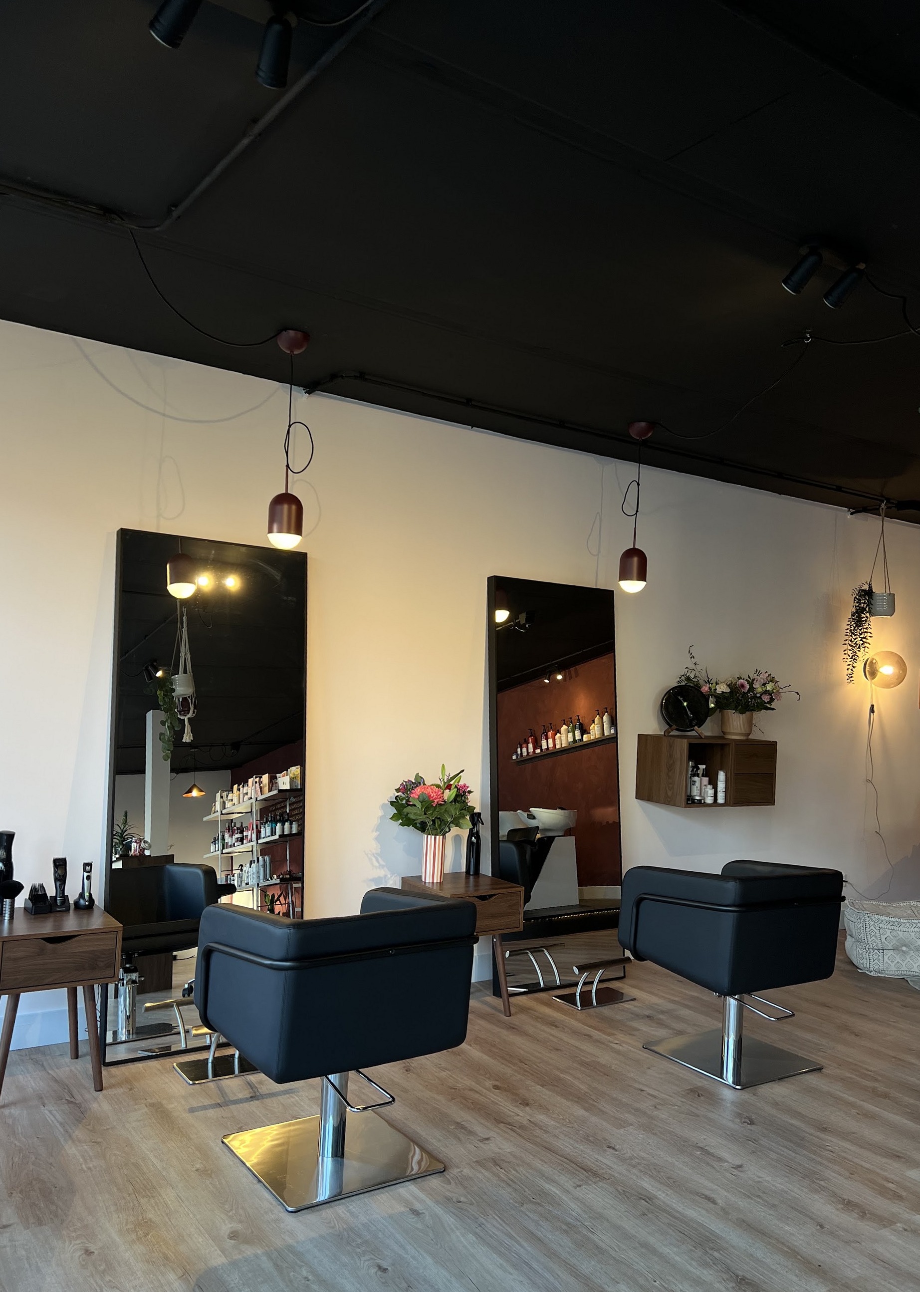De salon van Studio 38: twee zwarte stoelen voor hoge spiegels, houten bijzettafels met bloemen en de terracotta muur in de spiegel